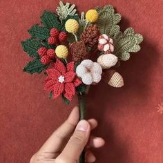 a hand holding a crocheted flower bouquet on top of a red cloth covered surface