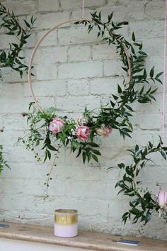 flowers and greenery are arranged around a circular wreath on a shelf in front of a brick wall