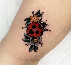 a ladybug tattoo with flowers and leaves on the leg