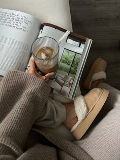 a person sitting on a couch reading a book and holding a drink in their hand