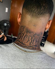 the back of a man's neck with his name tattooed on it, while another person sits in the background