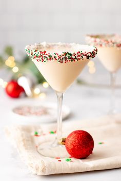 two martini glasses with sprinkles and a red ornament on the side