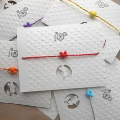 four white cards with red string attached to them and some orange beads on the strings