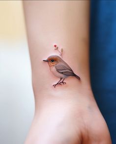 a small bird tattoo on the wrist of a woman's hand with tiny flowers