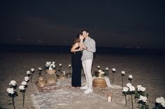 a man and woman kissing on the beach in front of some white flowers at night