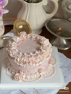 a pink cake sitting on top of a white platter next to a vase with flowers