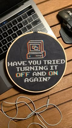 there is a cross stitch pattern on the table next to a laptop and headphones