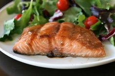 a white plate topped with salmon next to a green leafy salad and cherry tomatoes