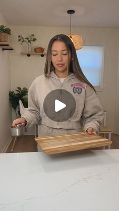 a woman standing in front of a counter holding a wooden tray