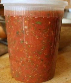 a plastic cup filled with salsa sitting on top of a wooden table