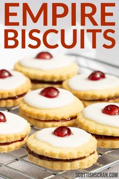 some cookies with white icing and cherries are on a cooling rack for display