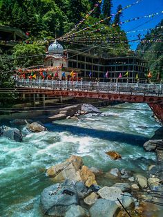 people are walking across a bridge over a river in the mountains with rocks and water