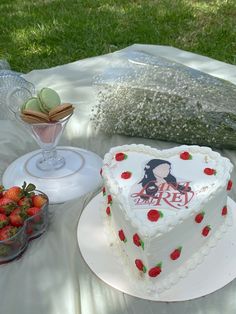 a heart shaped cake sitting on top of a table next to strawberries and cookies