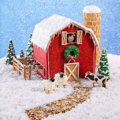 a red barn with snow on the roof and trees in front of it is decorated for christmas