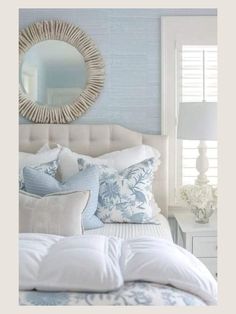 a white bed with blue and white pillows on top of it next to a round mirror