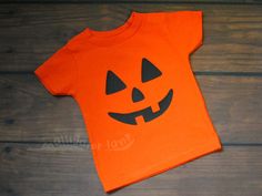 an orange shirt with a jack - o'- lantern face on it sitting on top of a wooden floor