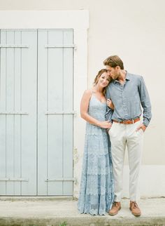 a man and woman standing next to each other in front of a white building with blue shutters