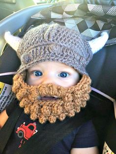 a young child wearing a knitted viking hat and beard in a car seat with the hood up