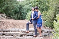 a man and woman standing next to each other on some rocks in the middle of a forest