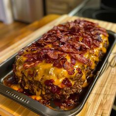 a meatloaf covered in cheese and bacon on top of a baking pan with a spatula