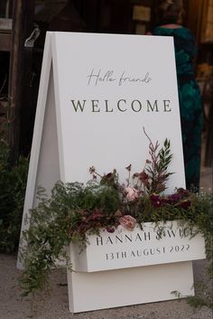 a welcome sign with flowers and greenery on it