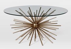 a glass table topped with wooden sticks and a circular glass top sitting on a white floor