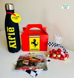 a table topped with candy and a red box next to a black bottle on top of it