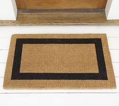 a door mat on the floor next to a wooden door with a brown and black border