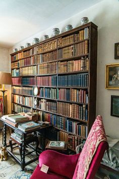 a living room filled with lots of books on top of a book shelf next to a red chair