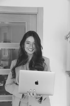 black and white photograph of a woman holding an apple laptop in front of her face