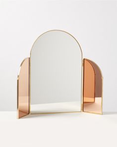 an arch shaped mirror on top of a white table next to a pink and gold shelf