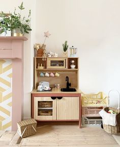 a toy kitchen with wooden furniture and plants on the top shelf, next to a pink fireplace