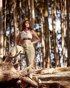 a woman standing on top of a fallen tree in the middle of a wooded area