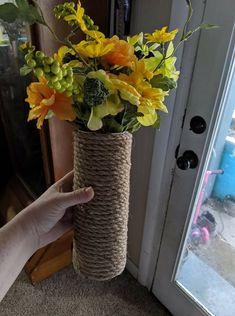 a hand holding a rope wrapped vase filled with flowers