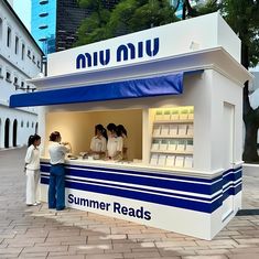 people standing in front of a kiosk selling summer reads