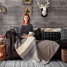 a woman sitting on a couch with a blanket over her and holding a coffee cup