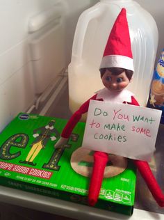 an elf is sitting on top of a cookie box and holding a sign that says do you want to make some cookies