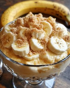 a dessert dish with bananas and crumbs in it sitting on a table next to a banana