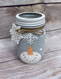 a mason jar decorated with snowflakes and an orange candle is sitting on a wooden table