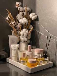 an assortment of skin care products sitting on a tray next to a vase with cotton