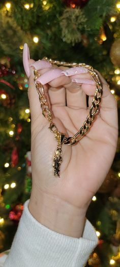 a person holding up a gold chain necklace in front of a christmas tree with lights