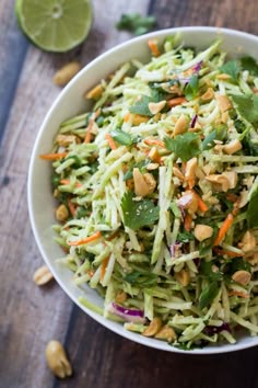 a white bowl filled with salad and nuts on top of a wooden table next to a fork