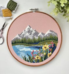 a cross stitch pattern with flowers and mountains in the background, on a pink hoop