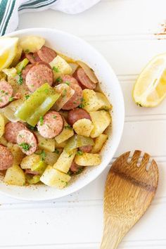 a white bowl filled with sausage and potatoes next to a wooden spoon on top of a table