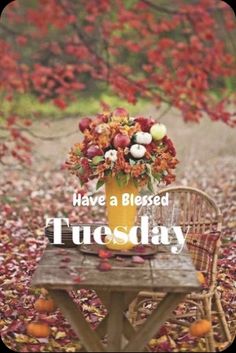 a vase with flowers sitting on top of a wooden table in the middle of leaves