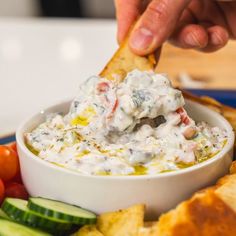 a person dipping some kind of food into a bowl with bread and cucumbers