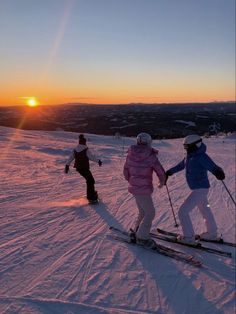 three people on skis in the snow at sunset or dawn, with one person skiing behind them