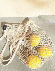 three lemons in a mesh bag sitting on the ground next to a concrete wall