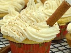 cupcakes with white frosting and cinnamon stick on top, sitting on a cooling rack