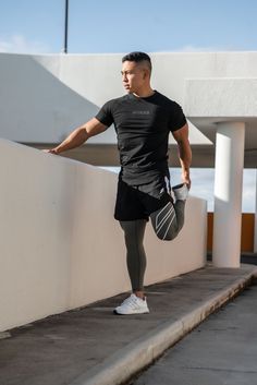 a man in black shirt and leggings leaning against wall with hand on hip